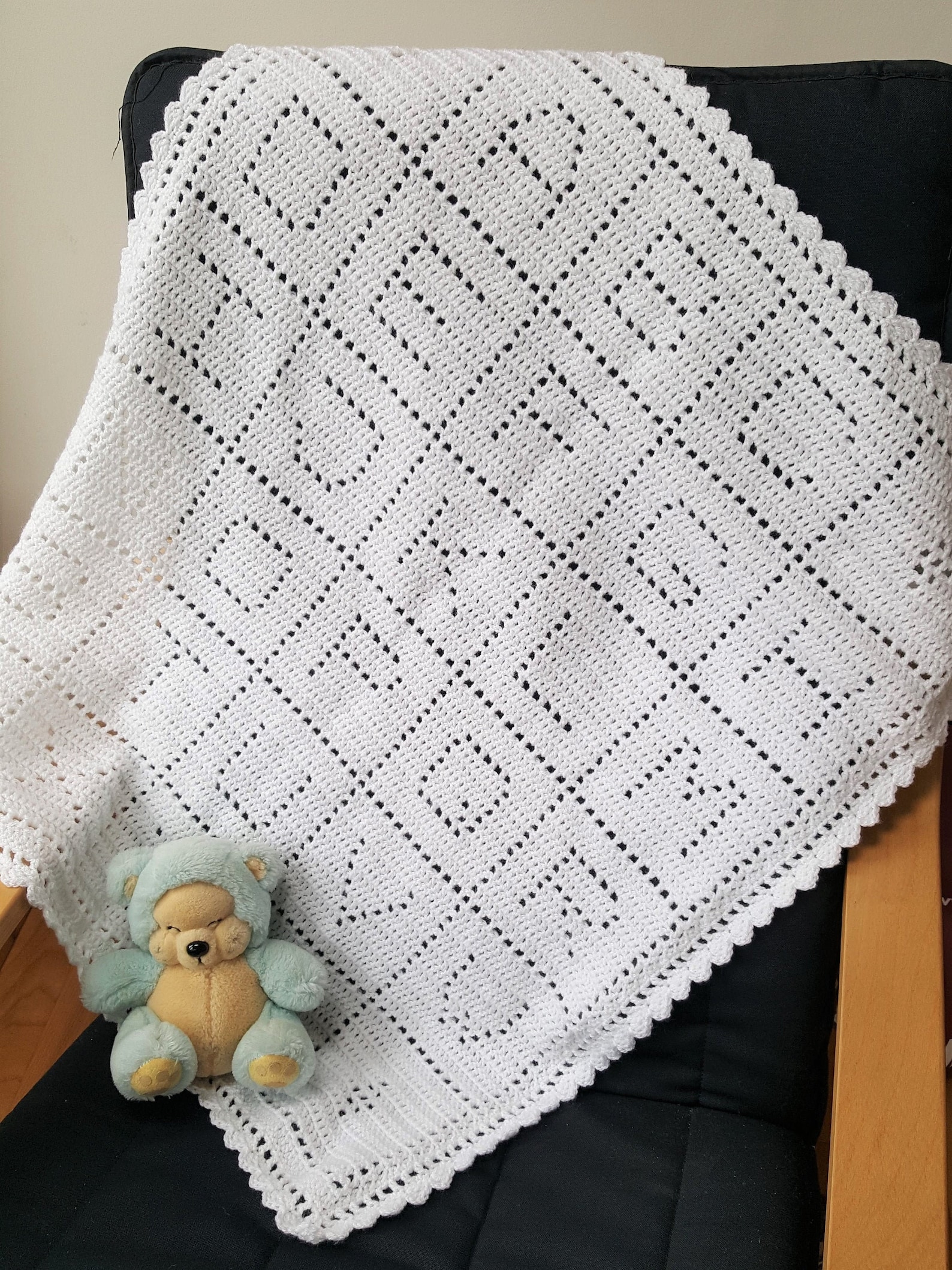 White filet crochet baby blanket with alphabet blocks and scalloped edging, folded with a stuffed bear