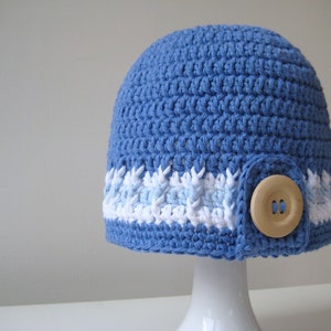 Puede incluir: Un gorro de punto azul con ribete blanco y azul claro y un bot&oacute;n de madera.