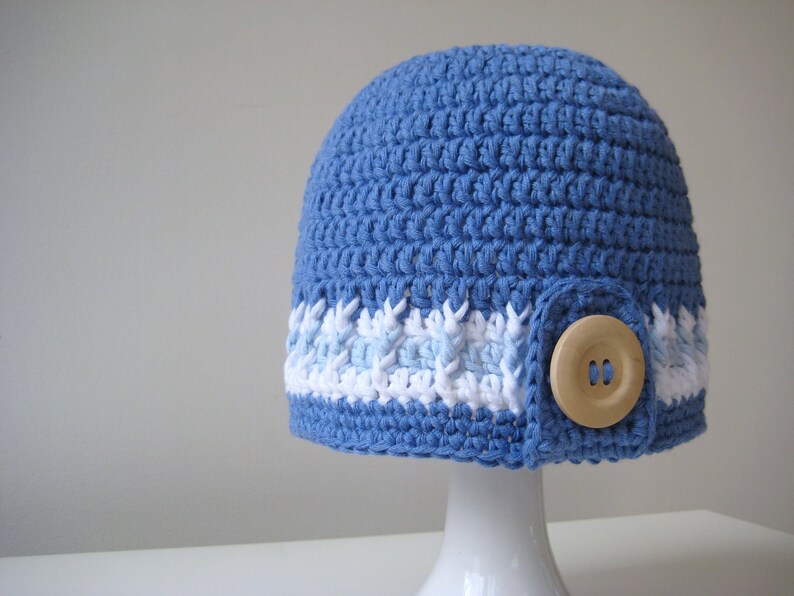 Puede incluir: Un gorro de punto azul con ribete blanco y azul claro y un bot&oacute;n de madera.