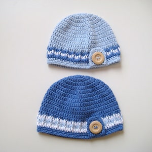 Puede incluir: Dos gorros de punto de ganchillo en tonos azules con detalles blancos y un bot&oacute;n de madera en cada uno.