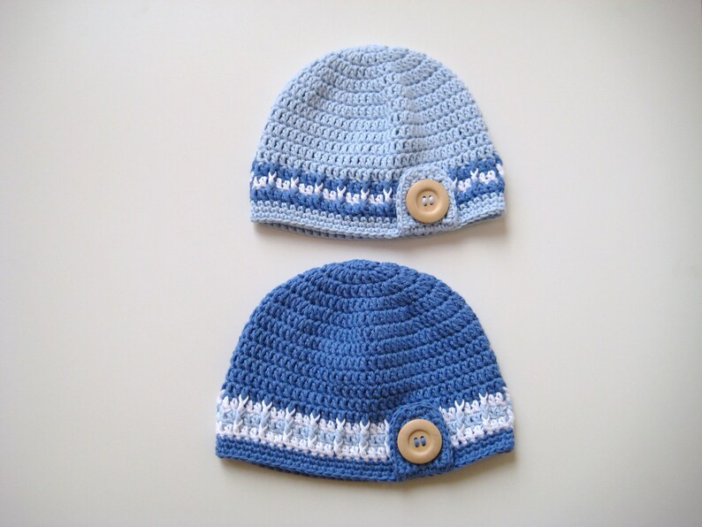 Puede incluir: Dos gorros de punto de ganchillo en tonos azules con detalles blancos y un bot&oacute;n de madera en cada uno.