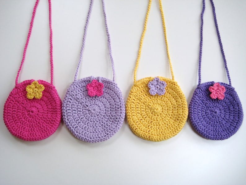 May include: Four crocheted purses with flower embellishments. The purses are pink, purple, yellow, and purple. Each purse has a long strap.