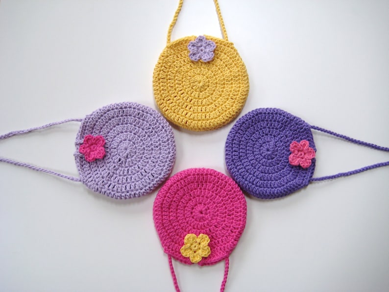 May include: Four crocheted purses with flower embellishments. The purses are in shades of yellow, purple, and pink.
