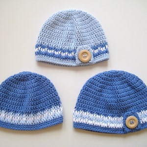 Puede incluir: Tres gorros de ganchillo en tonos azules con detalles blancos. Cada gorro tiene un bot&oacute;n en el lateral.