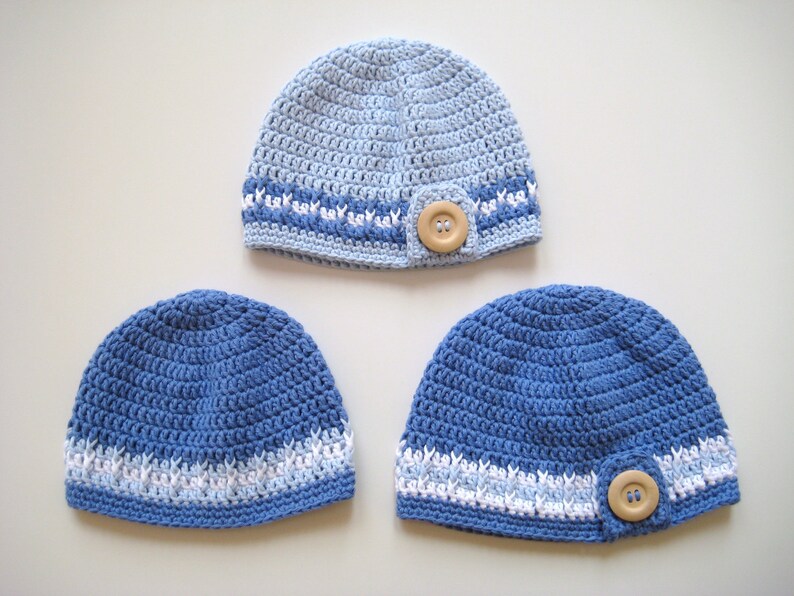 Puede incluir: Tres gorros de ganchillo en tonos azules con detalles blancos. Cada gorro tiene un bot&oacute;n en el lateral.
