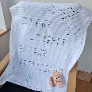 Könnte beinhalten: Weiße gehäkelte Babydecke mit einem Sternendesign und den Worten "Star Bright Star Bright" in der Mitte. Ein kleiner Teddybär sitzt auf der Decke.