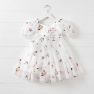 This enchanting strawberry birthday dress features exquisite, embroidered tulle adorned with strawberries, delicate bows, and a whimsical cake motif. The word "Strawberry" is beautifully embroidered throughout, creating a cohesive themed design perfect for first birthdays and milestone celebrations.