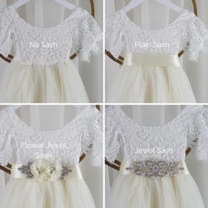 Op de afbeelding: Een witte kanten jurk met een tule rok, getoond in vier varianten: No Sash, Plain Sash, Flower Jewel Sash en Jewel Sash. Het kanten lijfje heeft korte mouwen en een ronde halslijn, terwijl de taille wordt geaccentueerd door verschillende sjerpen.