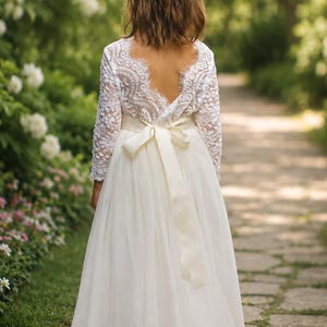 Flower girl dress in ivory tulle and lace shown from the back with long sleeves and satin sash.