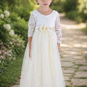Long sleeve flower girl dress in ivory lace and tulle shown full length on a young girl.