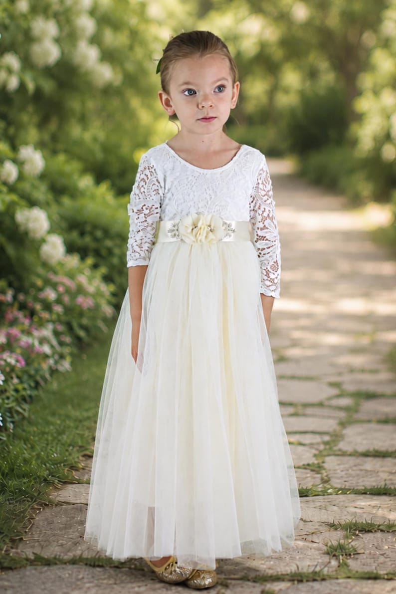 Long sleeve flower girl dress in ivory lace and tulle shown full length on a young girl.