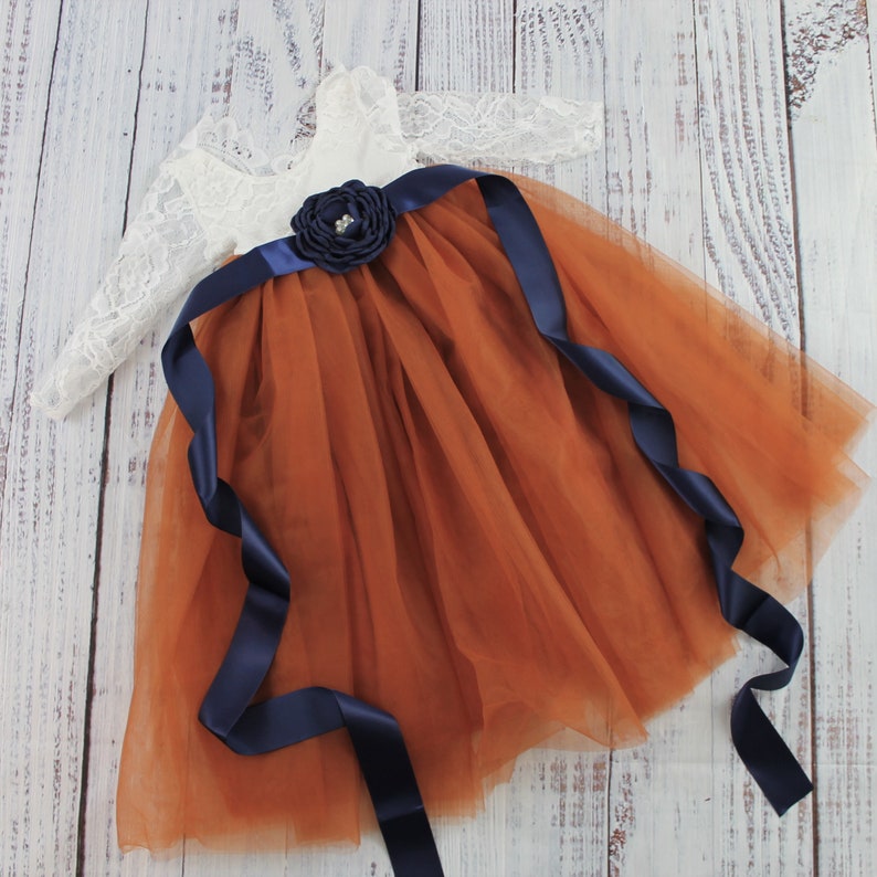 junior bridesmaid dress in burnt orange with navy blue sash and white lace long sleeve bodice.