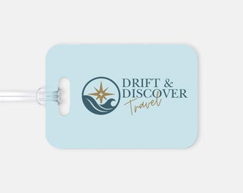 Op de afbeelding: Een lichtblauwe bagagelabel met de tekst "DRIFT & DISCOVER Travel" in marineblauw en goud. De tag heeft een cirkelvormig logo met een kompasroos en golven.