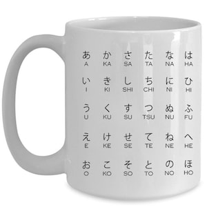 May include: White ceramic mug with a black Japanese hiragana chart printed on the front. The chart includes the Japanese characters for the sounds "a", "ka", "sa", "ta", "na", "ha", "i", "ki", "shi", "chi", "ni", "hi", "u", "ku", "su", "tsu", "nu", "fu", "e", "ke", "se", "te", "ne", "he", "o", "ko", "so", "to", "no", "ho".