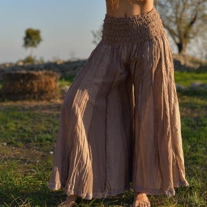 May include: A pair of wide-legged pants in a light brown color with a gathered elastic waistband. The pants have a flowing, relaxed fit and are made of a soft, lightweight fabric.