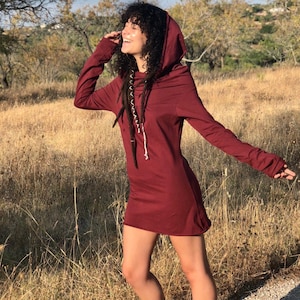 May include: A maroon hooded dress with long sleeves and a gathered neckline. The dress is made of a soft, comfortable fabric and has a relaxed fit.