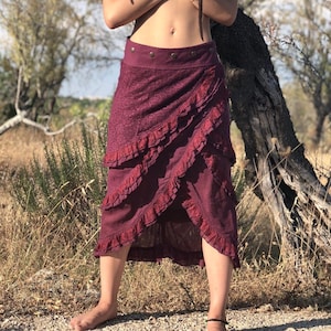 May include: A long burgundy skirt with multiple layers of ruffles. The skirt has a wide waistband with decorative buttons.