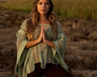 Può includere: Un poncho verde chiaro con un pannello frontale sfrangiato e motivi geometrici marroni sulle maniche, abbinato a leggings marroni scuri a tre quarti con lacci incrociati che si avvolgono attorno alla parte inferiore.