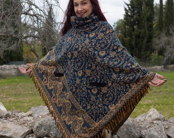 May include: A blue and gold patterned poncho with fringe trim. The poncho has a high neck and two pockets.