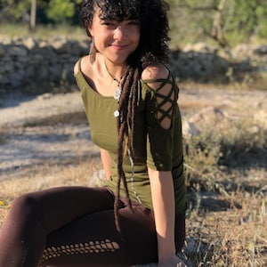 Pode incluir: Uma mulher com cabelo castanho encaracolado está vestindo uma blusa verde sem ombros com um design de cruzamento nas mangas. Ela também está vestindo leggings marrons com um padrão de renda.