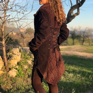 May include: A brown suede jacket with a lace back panel and a long, flowing tail. The jacket has a fitted bodice and a relaxed fit in the sleeves. The lace panel is tied with a brown ribbon at the waist.