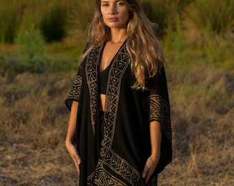 Può includere: Un kimono nero aperto sul davanti con un motivo geometrico color marrone chiaro lungo i risvolti e i bordi delle maniche. Il capo presenta maniche ampie e larghe e una silhouette lunga e fluida che si sovrappone a un top nero sottostante.