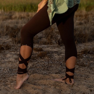 Könnte beinhalten: Braune Leggings mit einem einzigartigen Design mit einem Ausschnitt am Knöchel und einem braunen Band, das um das Bein gebunden ist. Die Leggings sind aus einem weichen, dehnbaren Stoff.