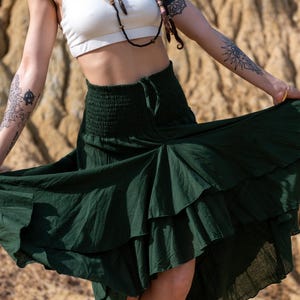 以下が含まれることがあります： ダークグリーンの、ティアードフリルデザインの流れるようなスカート。 スカートはシャーリングウエストとハイローヘムラインです。 軽量生地で作られており、暖かい季節に最適です。 ボヘミアン衣料品コレクションの一部です。