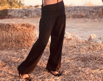 May include: A woman wearing a black strapless top with a beaded necklace and black wide-leg pants. She is standing in a field of hay.