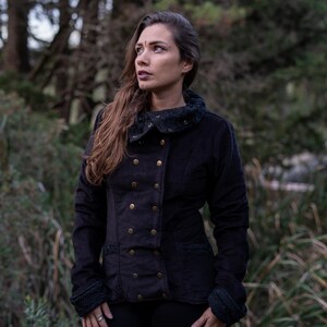 May include: A black double-breasted jacket with a high collar and gold buttons. The jacket has a fitted silhouette and is made of a soft, textured fabric.