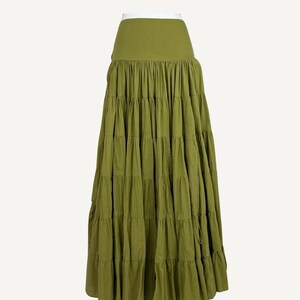 May include: Matcha green tiered maxi skirt. The skirt features a high waist and multiple layers of fabric, creating a flowing silhouette. The skirt is a solid color and has a drawstring closure. The text "Matcha Green" is in the upper right corner.