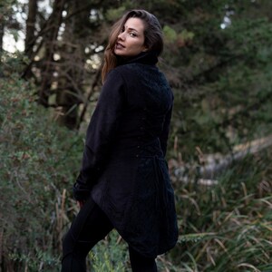May include: A black, long-sleeved jacket with a high collar and a lace-up back. The jacket has a fitted silhouette and a long, flowing tail.