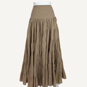 May include: A long, tiered skirt in a taupe color. The skirt has a high waist and a flowing, layered design. The fabric appears to be a lightweight material, suitable for warmer weather. The word "Taupe" is in the upper right corner.