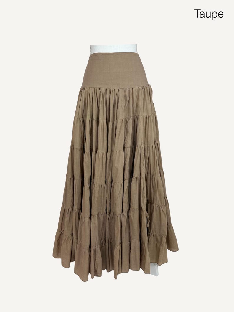 May include: A long, tiered skirt in a taupe color. The skirt has a high waist and a flowing, layered design. The fabric appears to be a lightweight material, suitable for warmer weather. The word "Taupe" is in the upper right corner.