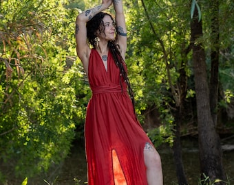Peut inclure: Une longue robe rouge fluide avec un col halter et une fente haute. La robe est faite d'un tissu léger et est portée à l'extérieur. Le modèle a des tatouages et de longs cheveux noirs. L'arrière-plan est une forêt verte.