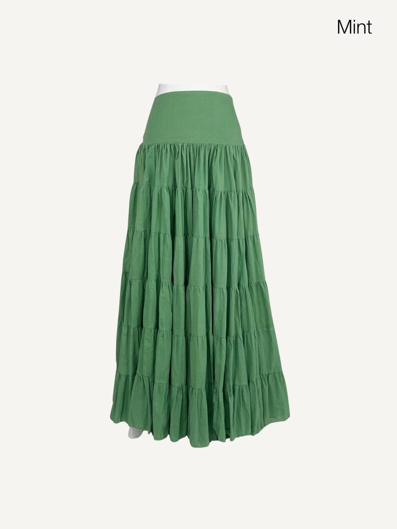 May include: A mint green tiered maxi skirt. The skirt has a wide waistband and multiple layers of gathered fabric, creating a flowing silhouette. The skirt is made of a lightweight material and is suitable for casual wear.