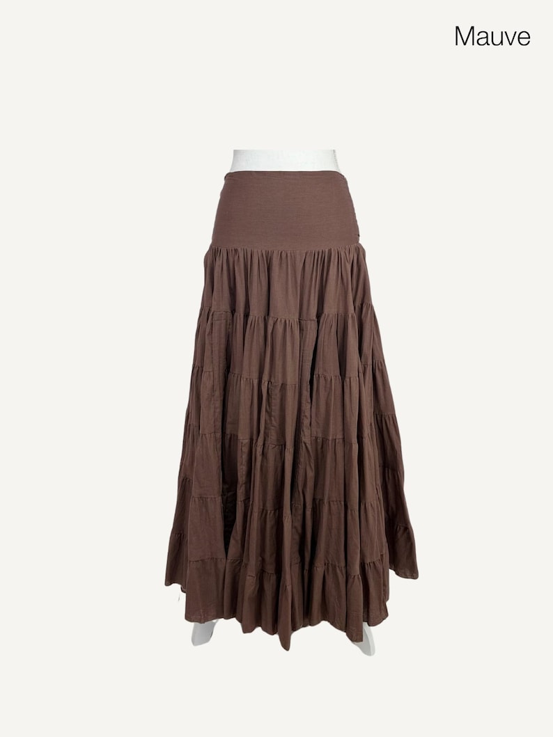 May include: Mauve tiered maxi skirt. The skirt features a wide, solid-colored waistband and multiple horizontal tiers that create a flowing, full silhouette. The skirt is a solid mauve color and is displayed on a white background.