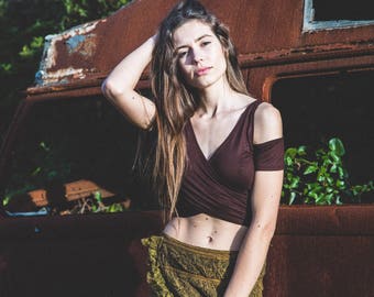 May include: A woman wearing a burgundy wrap top and a green lace skirt. The top has short sleeves and a V-neck. The skirt has a ruffled hem. The background features a rusty vehicle.