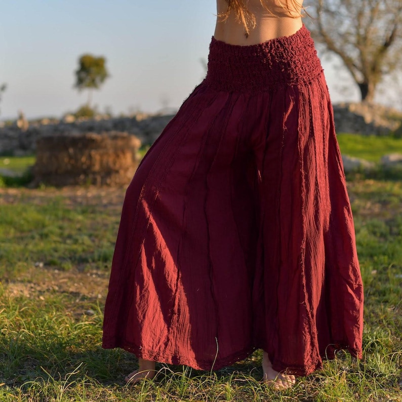 May include: A pair of wide-legged, burgundy pants with a gathered elastic waistband. The pants are made of a soft, flowing fabric and have a slightly flared hem.