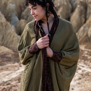 May include: A green knitted cardigan with a brown geometric pattern lining. The cardigan has a relaxed fit and long sleeves.
