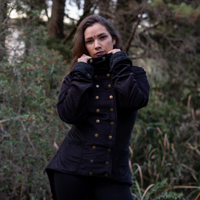 May include: A black, long-sleeved jacket with a high collar and gold buttons. The jacket has a fitted silhouette and a slightly longer back hem.