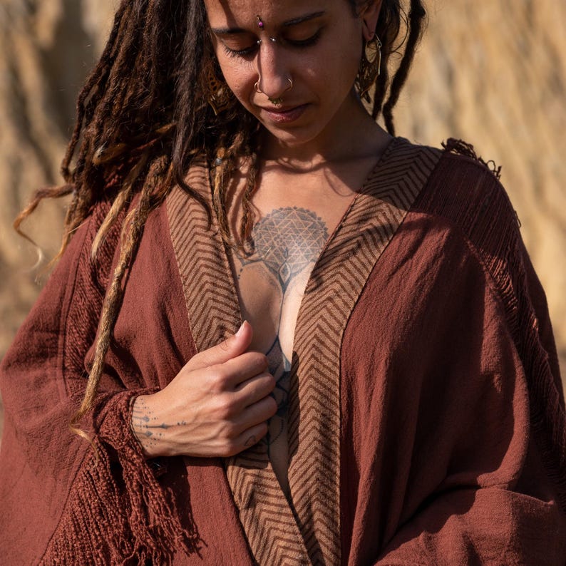 May include: A rust-colored, open-front robe with a brown chevron pattern along the edges. The robe has long sleeves and a fringed edge on the sleeve. The fabric appears to be a soft, woven material.