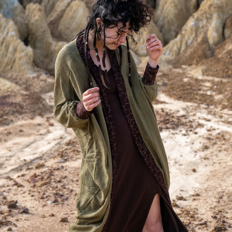 May include: A long, olive green cardigan with a brown, geometric pattern lining. The cardigan has a relaxed fit and long sleeves.