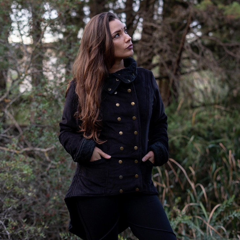 May include: A black quilted jacket with a high collar and gold buttons. The jacket has a long, flowing style and is worn by a person standing in a forest.