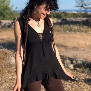 Può includere: Un top nero senza maniche con un dettaglio di pizzo sul davanti. Il top ha un orlo a balze ed è indossato con leggings marroni.