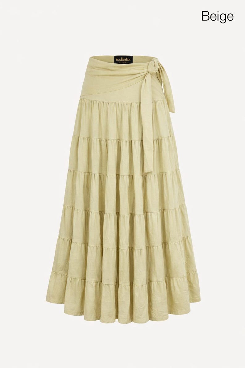 May include: A beige, tiered maxi skirt with a wrap-around waist and tie closure. The skirt has a flowing, layered design and is made of a light-colored fabric. The word "Beige" is in the upper right corner.