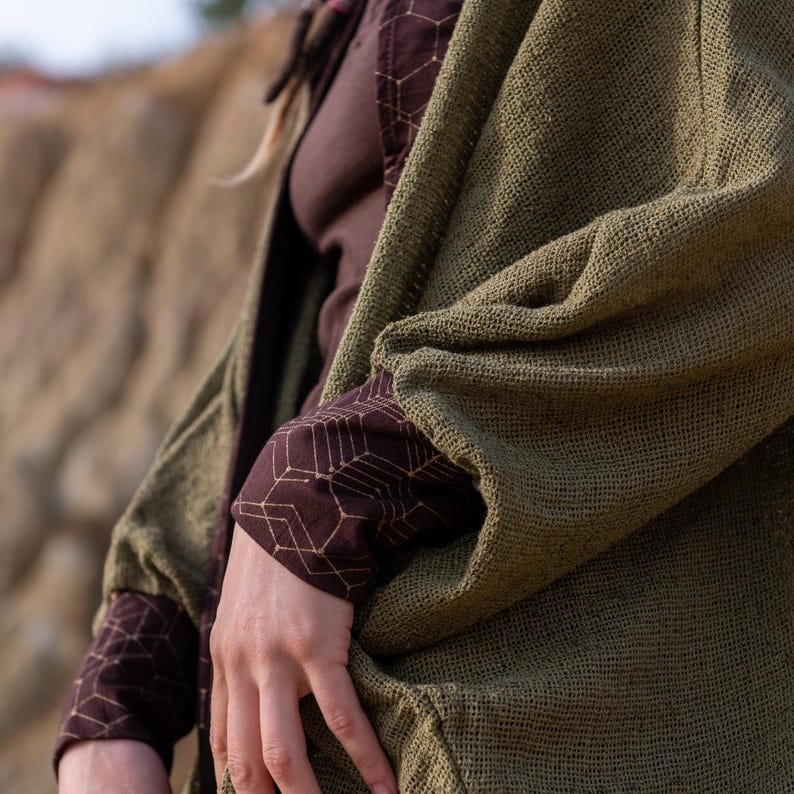 May include: A green cardigan with a textured weave. The cardigan has a geometric pattern on the sleeves and is worn over a brown shirt.