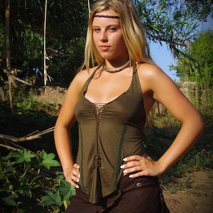 Peut inclure: Une femme porte un haut dos nu et une jupe. Le haut dos nu vert olive a un devant lacé et une bordure vert foncé. La jupe marron a un ourlet en dentelle. Elle porte également un bandeau noir et un collier doré.