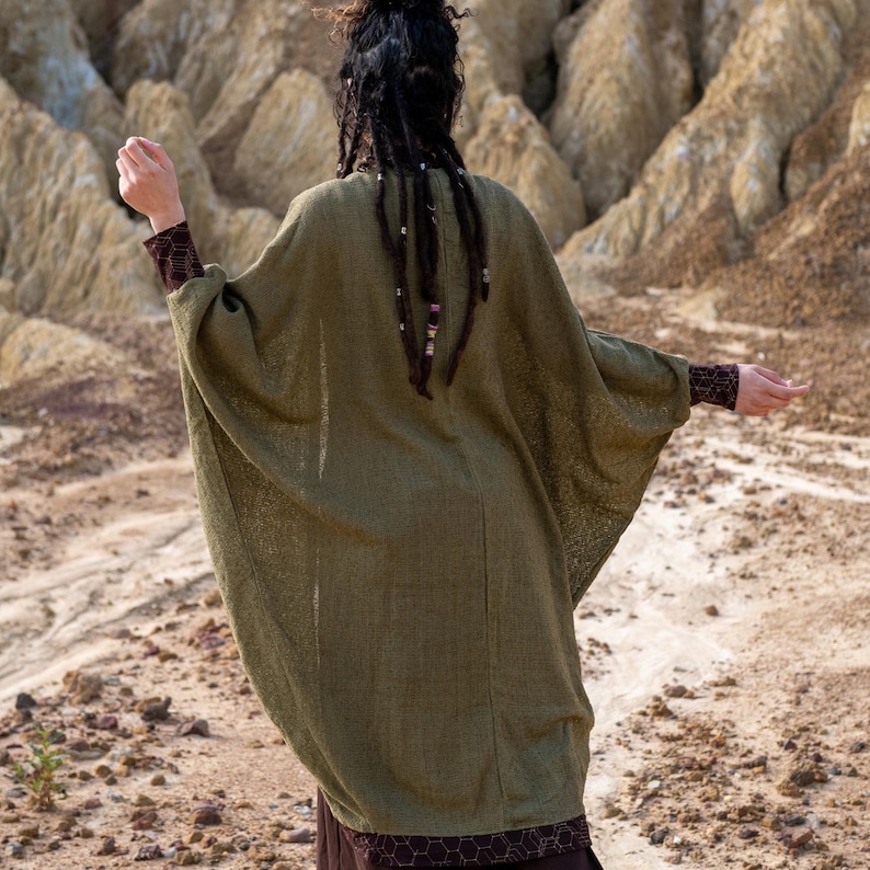 May include: A person wearing a long, loose-fitting, olive green cardigan with a brown and black patterned skirt.