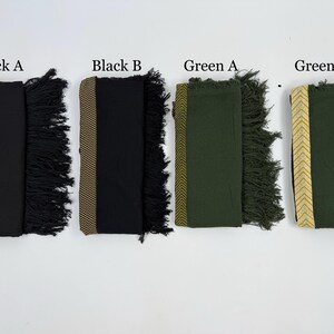 May include: Four folded scarves in black and green, each with a decorative border and fringe. The scarves are labeled "Black A", "Black B", "Green A", and "Green B". The borders feature gold and tan chevron or geometric patterns.